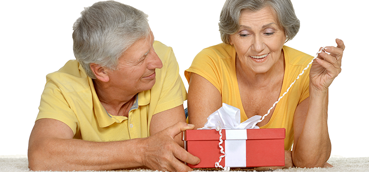 Mature couple resting on their elbows as woman opens a gift box