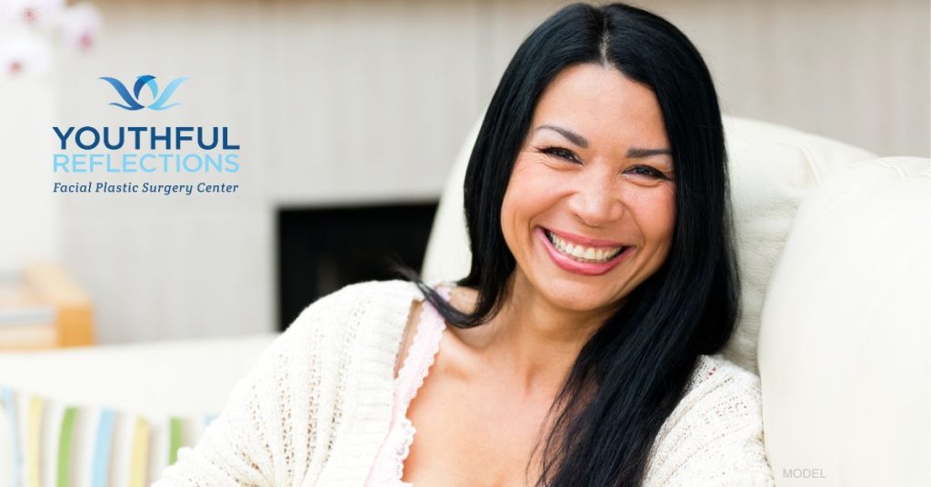 A woman with brown hair is sitting and smiling looking forward. (model)