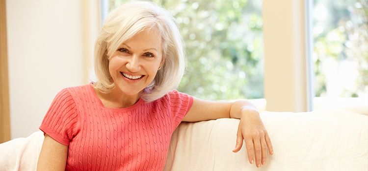 Middle aged woman smiling and sitting casually on white sofa in home