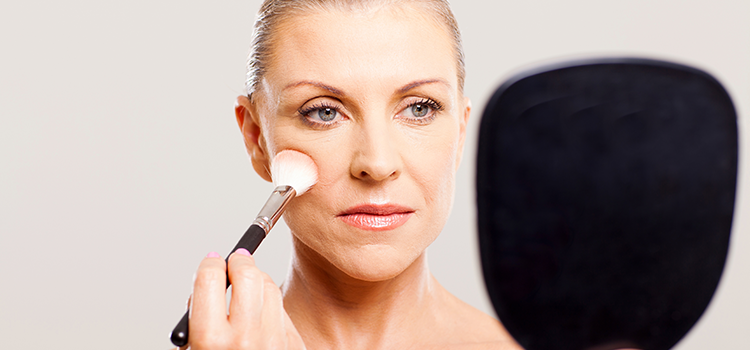 Woman looking at hand held mirror and applying makeup with brush