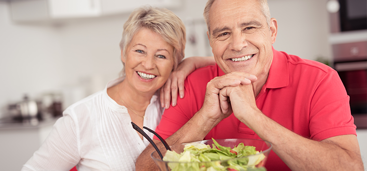 Mature couple smiling at camera with salad