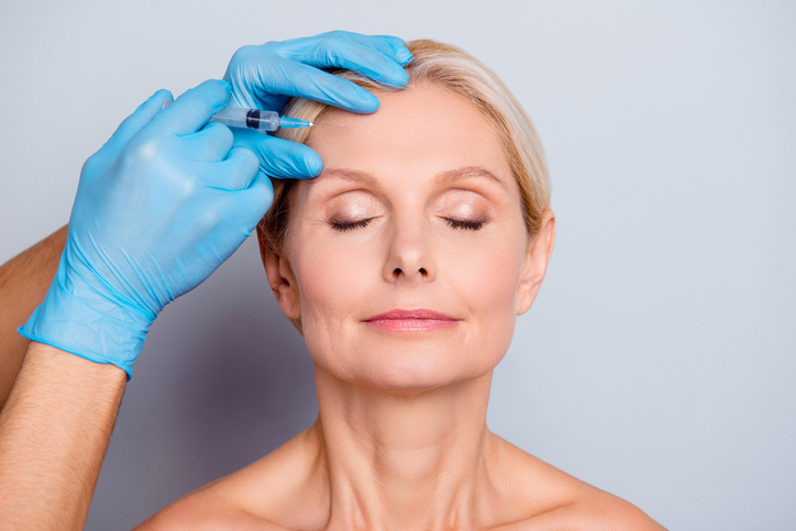 Woman seen from shoulders up with eyes closed as she gets Botox injection in forehead