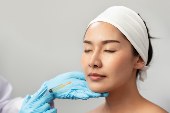 Gloved hand holding syringe preparing to inject young, attractive woman's lip with filler