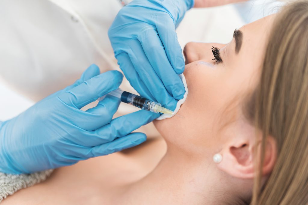 Gloved hands preparing to inject filler into young woman's face.