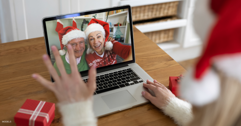 Woman in santa hat waving while having a videocall with senior couple in santa hats on laptop at home.