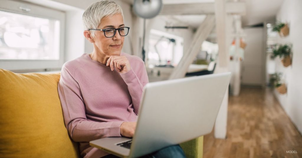 Mature woman (model) looking at before and after photos on a laptop.