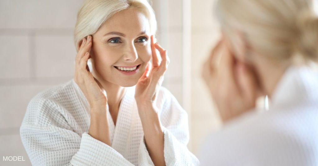 A mature woman looking at her face in the mirror (model)
