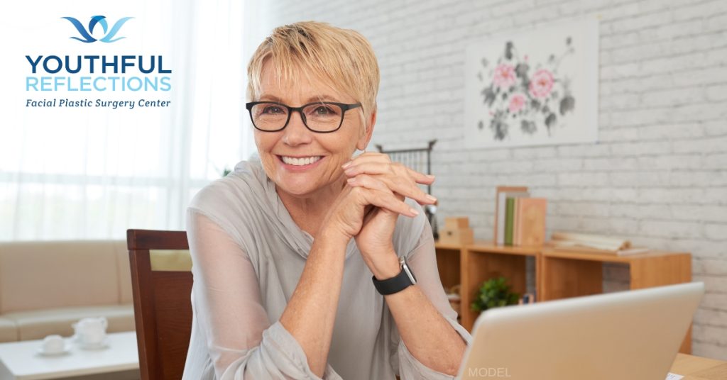Woman in her late sixties smiling at her computer desk (model)