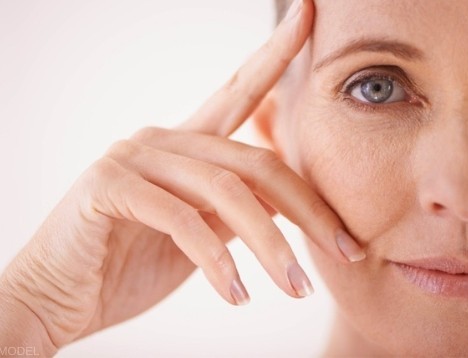 Close-up of a mature woman gently touching the skin around her eye with two fingers (model)